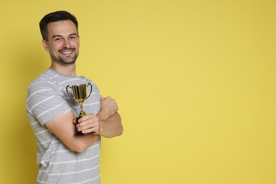 Photo of Happy winner with golden trophy cup on yellow background, space for text