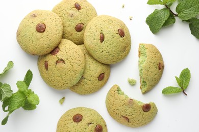 Photo of Delicious chocolate chip cookies and mint leaves on white table, flat lay