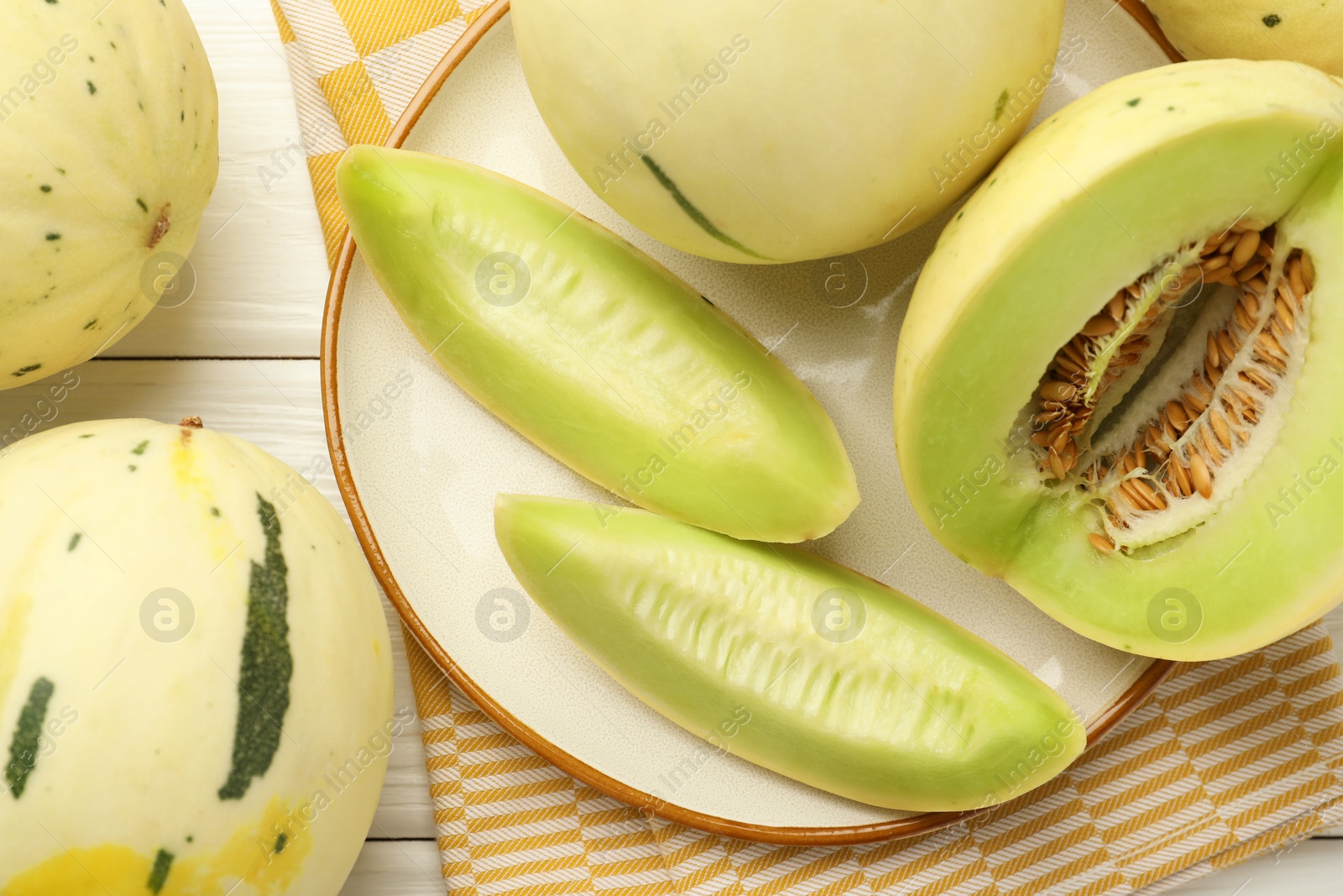 Photo of Fresh whole and cut honeydew melons on white wooden table, flat lay