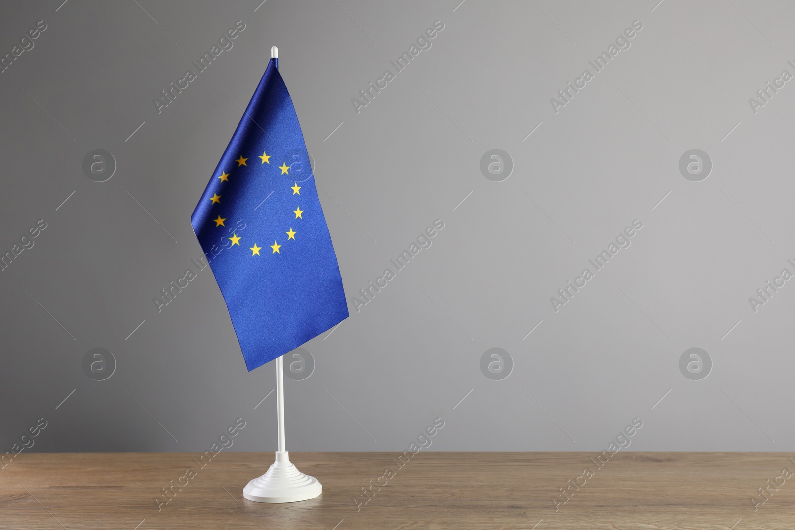 Photo of One flag of European Union on wooden table against grey background. Space for text