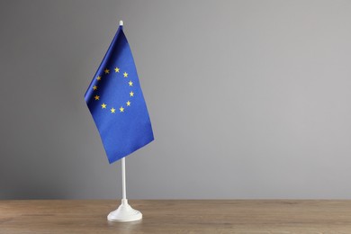 Photo of One flag of European Union on wooden table against grey background. Space for text