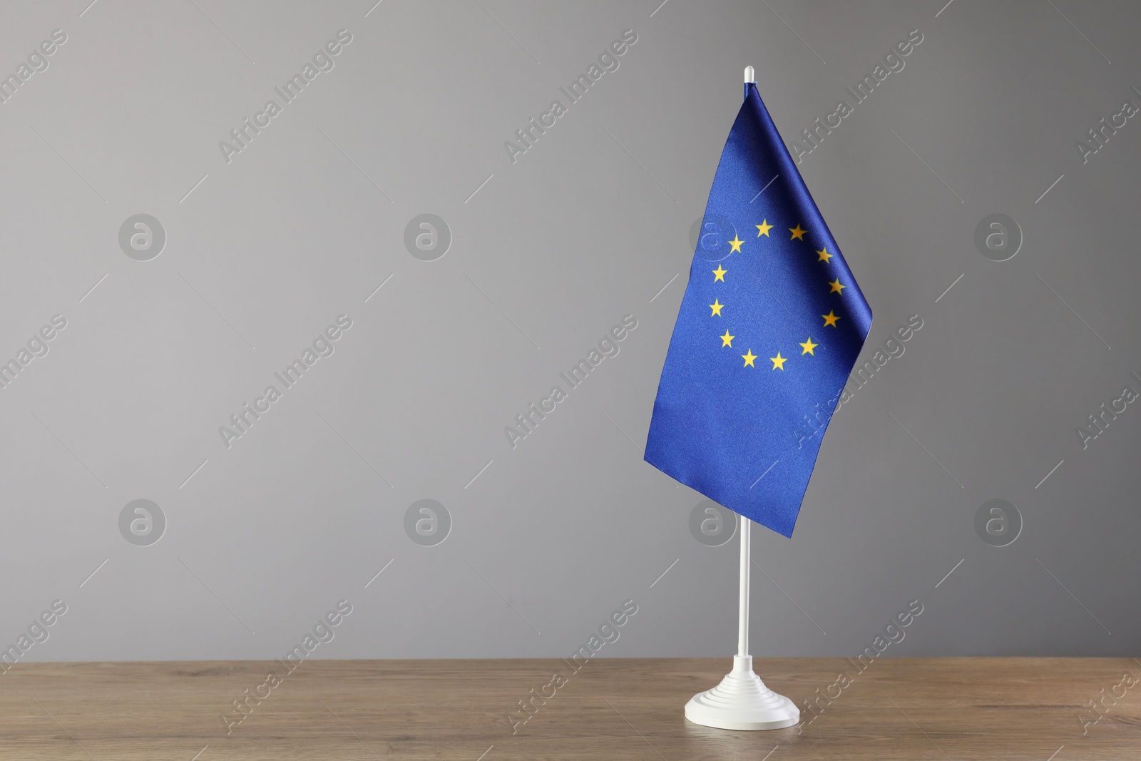 Photo of One flag of European Union on wooden table against grey background. Space for text