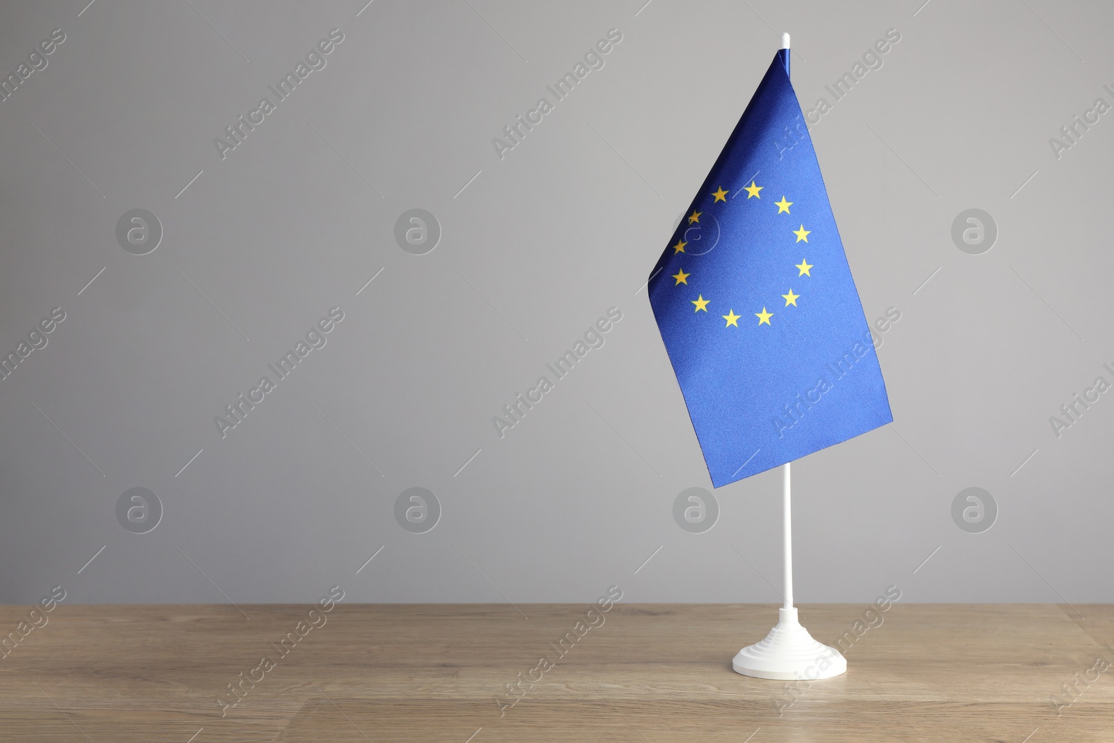 Photo of One flag of European Union on wooden table against grey background. Space for text