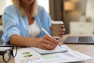 Photo of Budget planning. Woman with coffee taking notes at table indoors, closeup