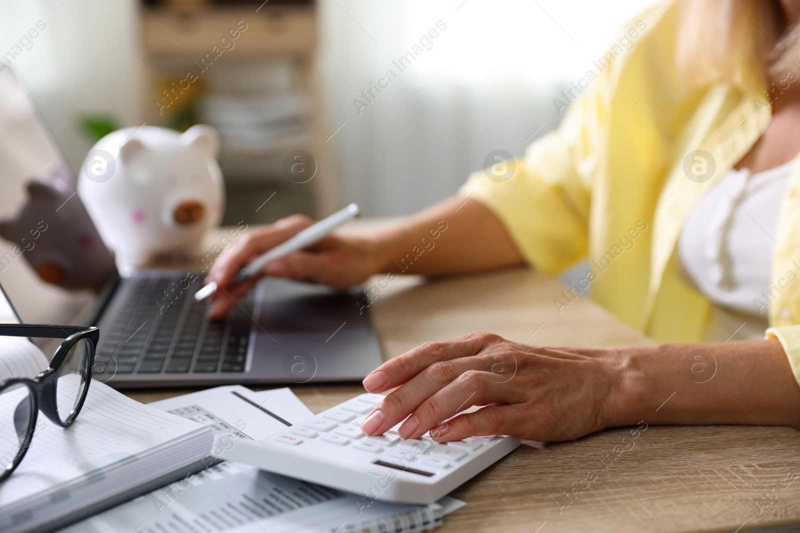 Photo of Budget planning. Woman working on laptop while using calculator at table indoors, closeup