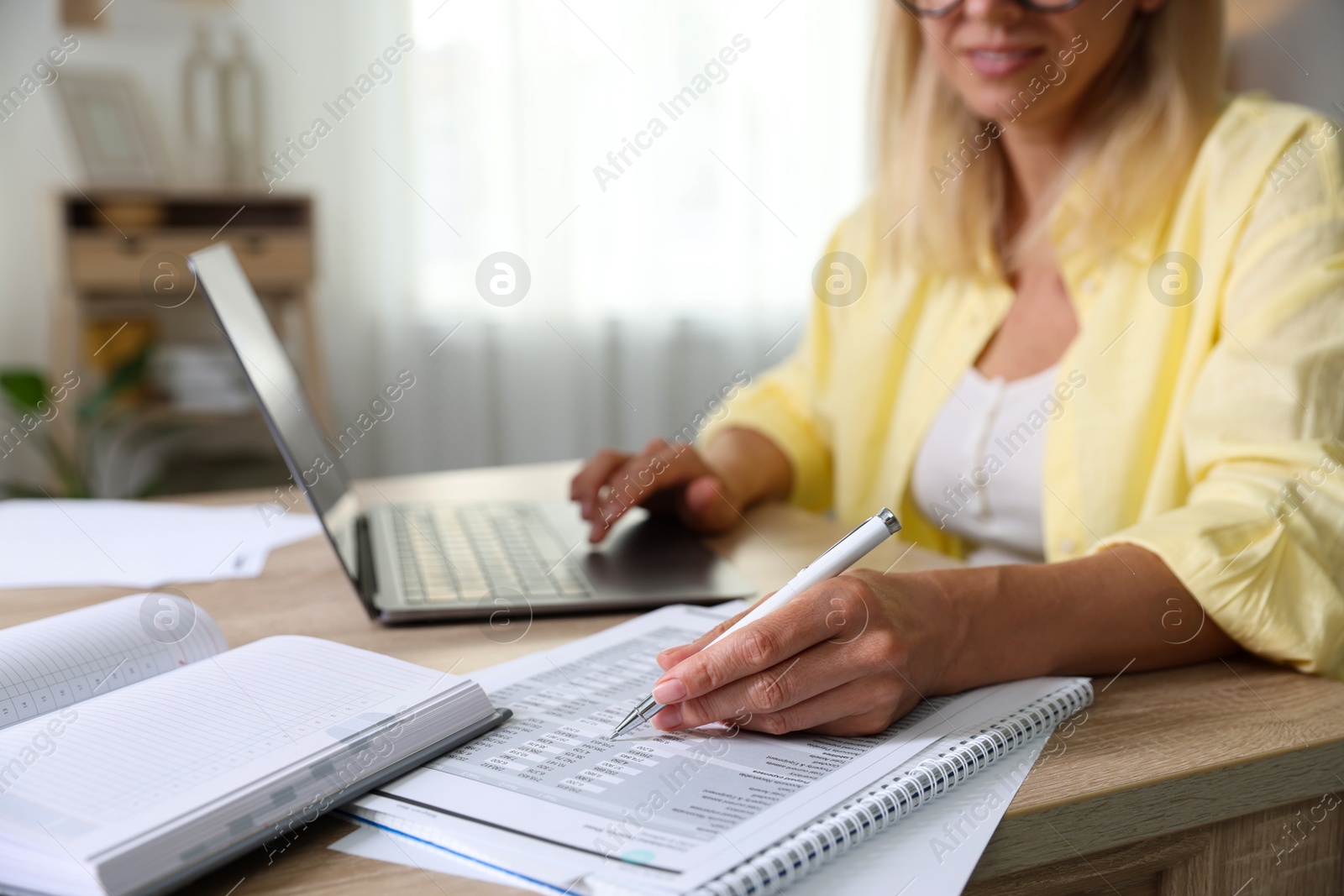 Photo of Budget planning. Woman using laptop while working with accounting documents at table indoors, closeup