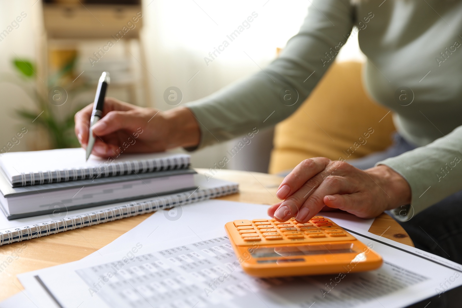 Photo of Budget planning. Woman using calculator while working with accounting documents at table indoors, closeup