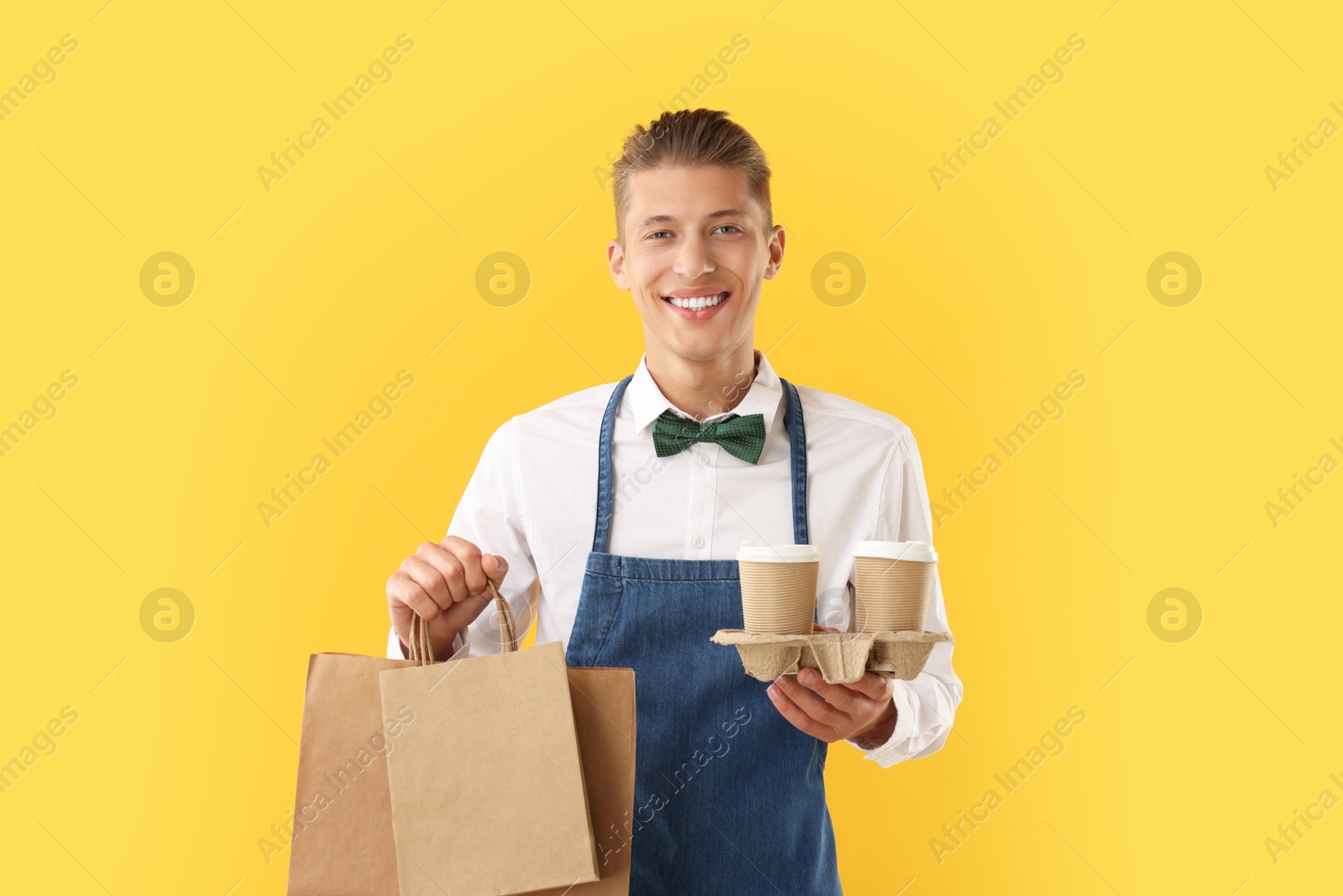 Photo of Fast-food worker with paper bags and cups on orange background