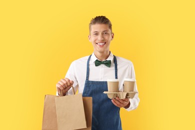 Photo of Fast-food worker with paper bags and cups on orange background