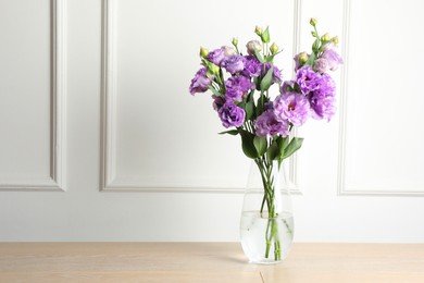 Photo of Vase with beautiful eustoma flowers on wooden table, space for text