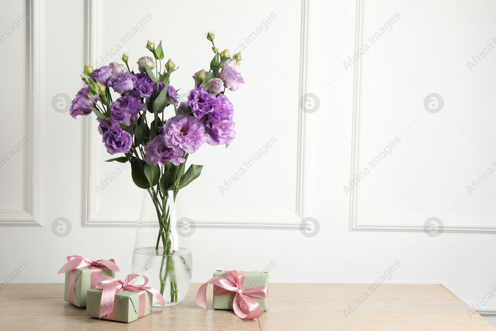 Photo of Vase with beautiful eustoma flowers and gift boxes on wooden table, space for text