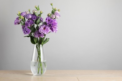 Photo of Vase with beautiful eustoma flowers on wooden table, space for text