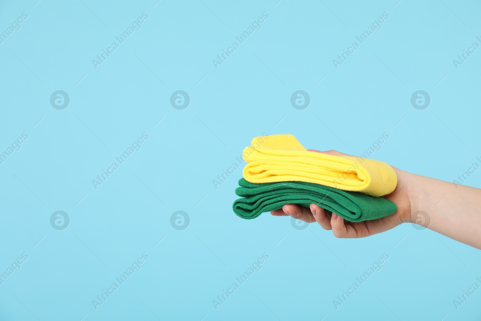 Photo of Woman holding bright folded socks on light blue background, closeup. Space for text