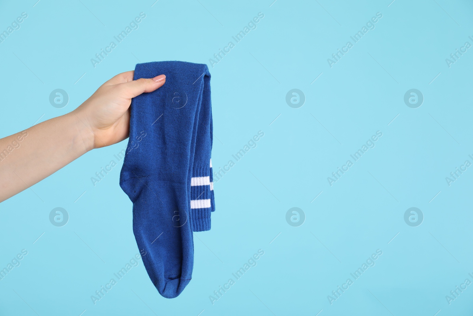 Photo of Woman holding pair of socks on light blue background, closeup. Space for text