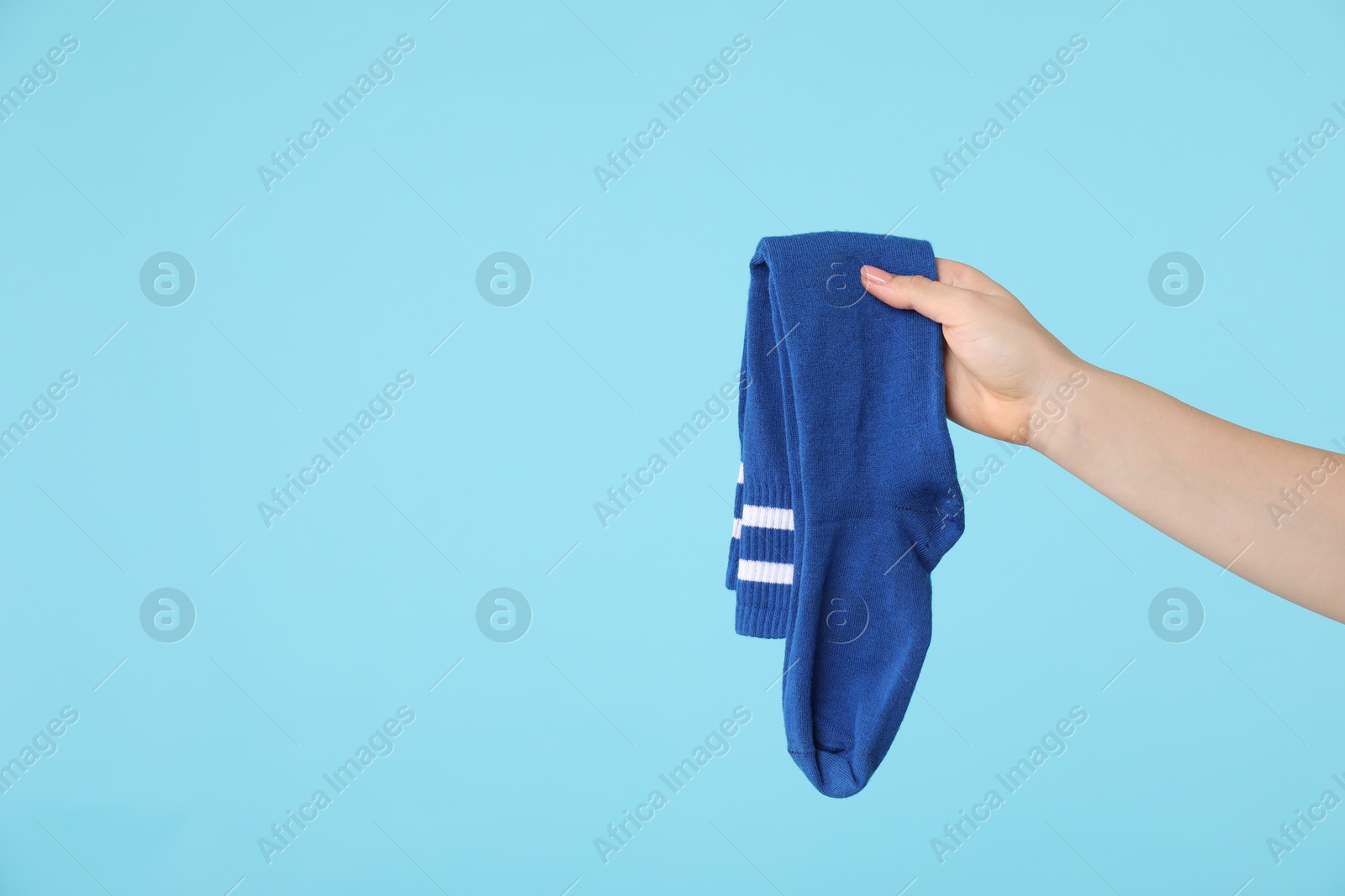 Photo of Woman holding pair of socks on light blue background, closeup. Space for text