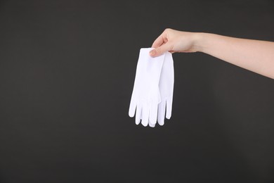 Photo of Woman holding pair of white gloves on black background, closeup. Space for text