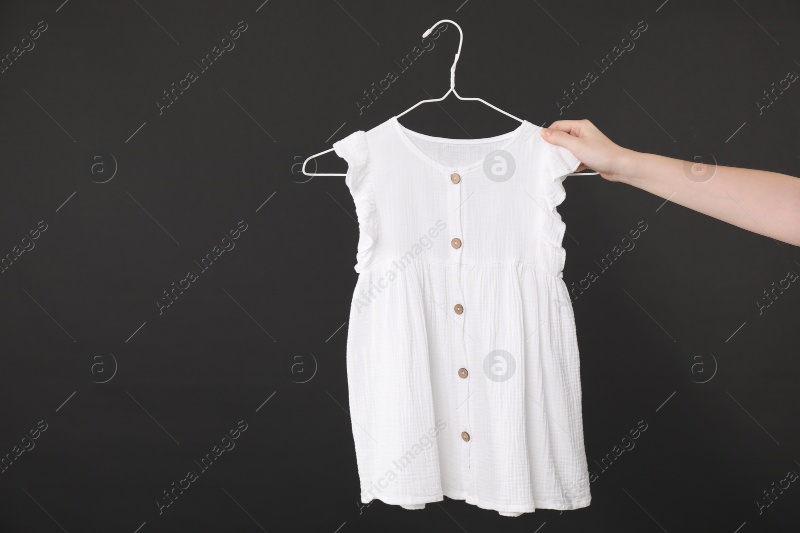 Photo of Woman holding hanger with white baby dress on black background, closeup. Space for text