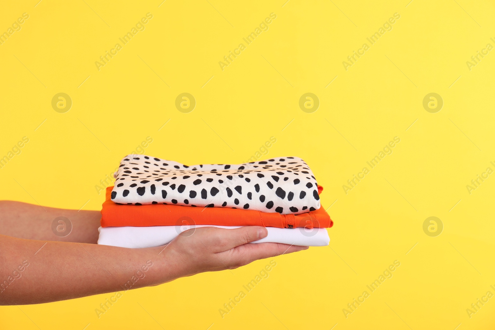 Photo of Woman holding stack of clothes on yellow background, closeup. Space for text