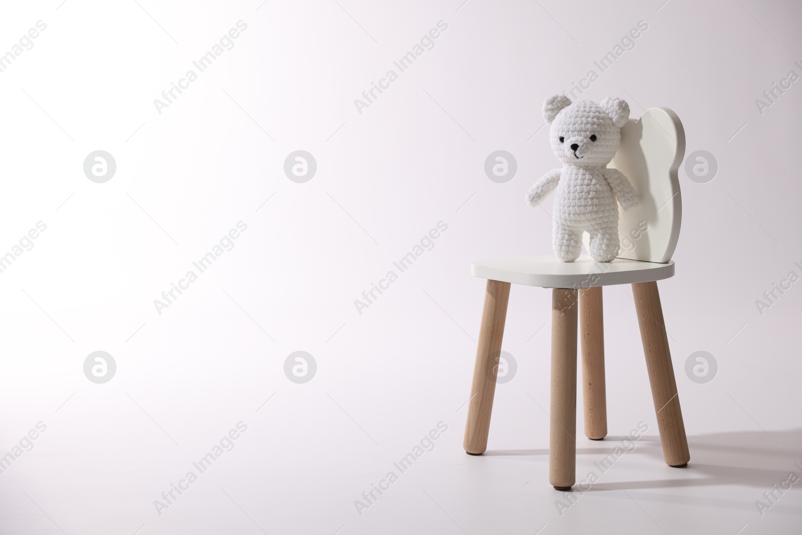 Photo of Cute crocheted bear on wooden chair against white background, space for text