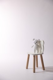 Photo of Cute crocheted bear on wooden chair against white background, space for text