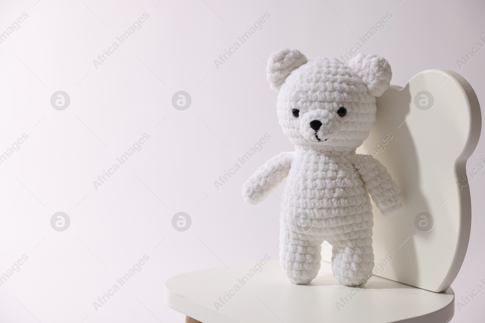 Photo of Cute crocheted bear on wooden chair against white background, space for text