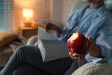 Photo of Woman reading book at home, focus on apple