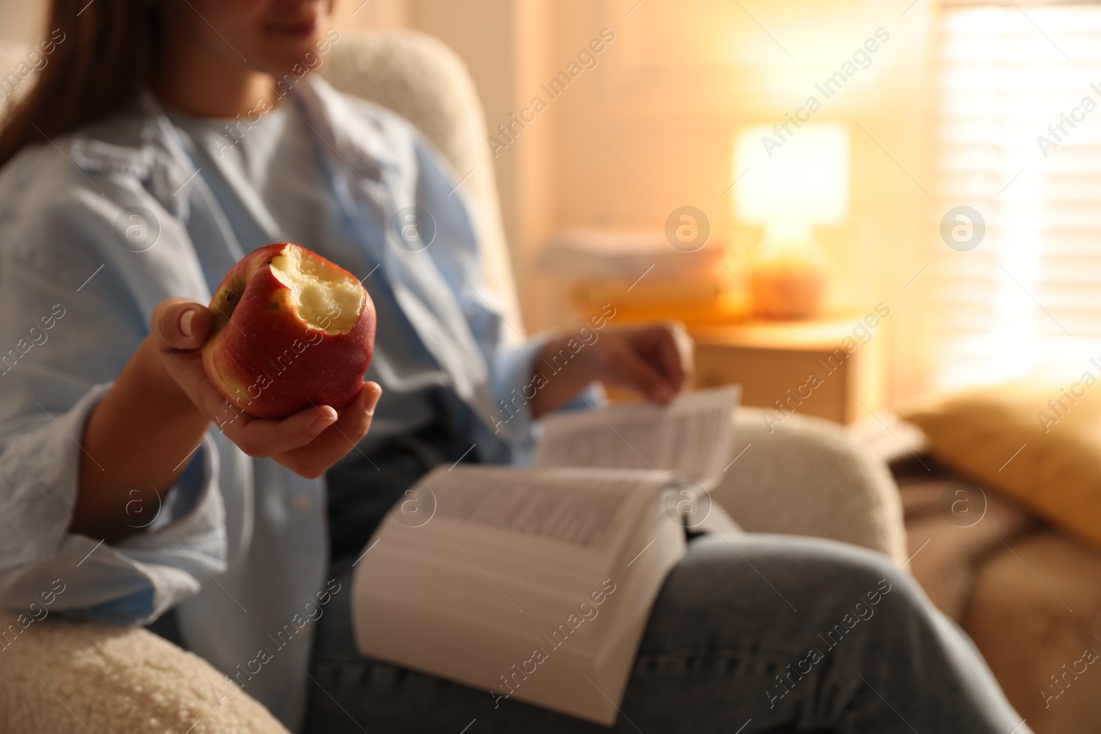 Photo of Woman reading book at home, focus on apple