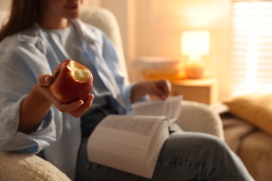 Photo of Woman reading book at home, focus on apple