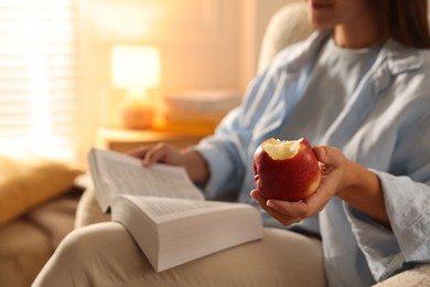 Woman reading book at home, focus on apple