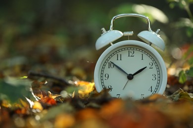 Photo of Alarm clock on fallen dry leaves outdoors, closeup. Space for text