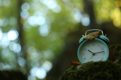 Photo of Alarm clock on green moss outdoors, closeup. Space for text