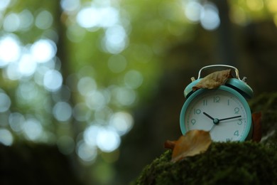 Photo of Alarm clock on green moss outdoors, closeup. Space for text