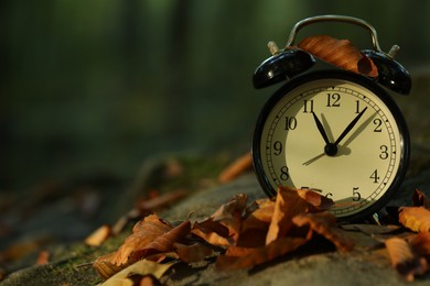 Photo of Alarm clock on fallen dry leaves and stones outdoors, closeup. Space for text