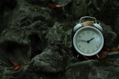 Photo of Alarm clock on stones outdoors, closeup. Space for text