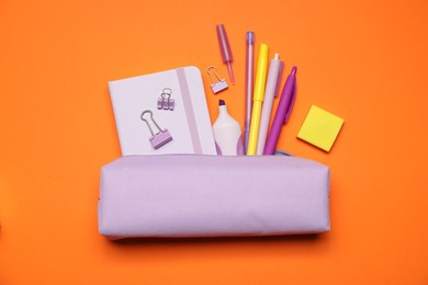 Photo of Pencil case and different stationery on orange background, flat lay