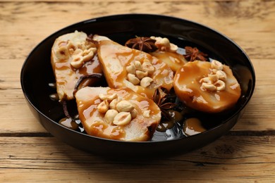 Photo of Delicious pears with caramel sauce, nuts and anise stars on wooden table, closeup