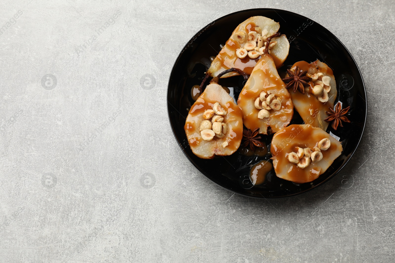 Photo of Delicious pears with caramel sauce, nuts and anise stars on grey table, top view. Space for text