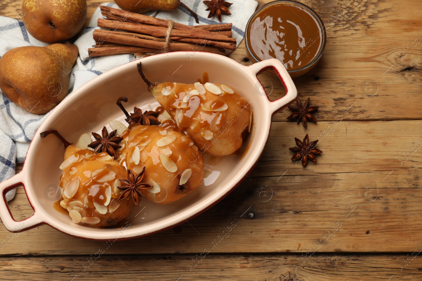 Photo of Delicious pears with caramel sauce, almond flakes and spices on wooden table, top view