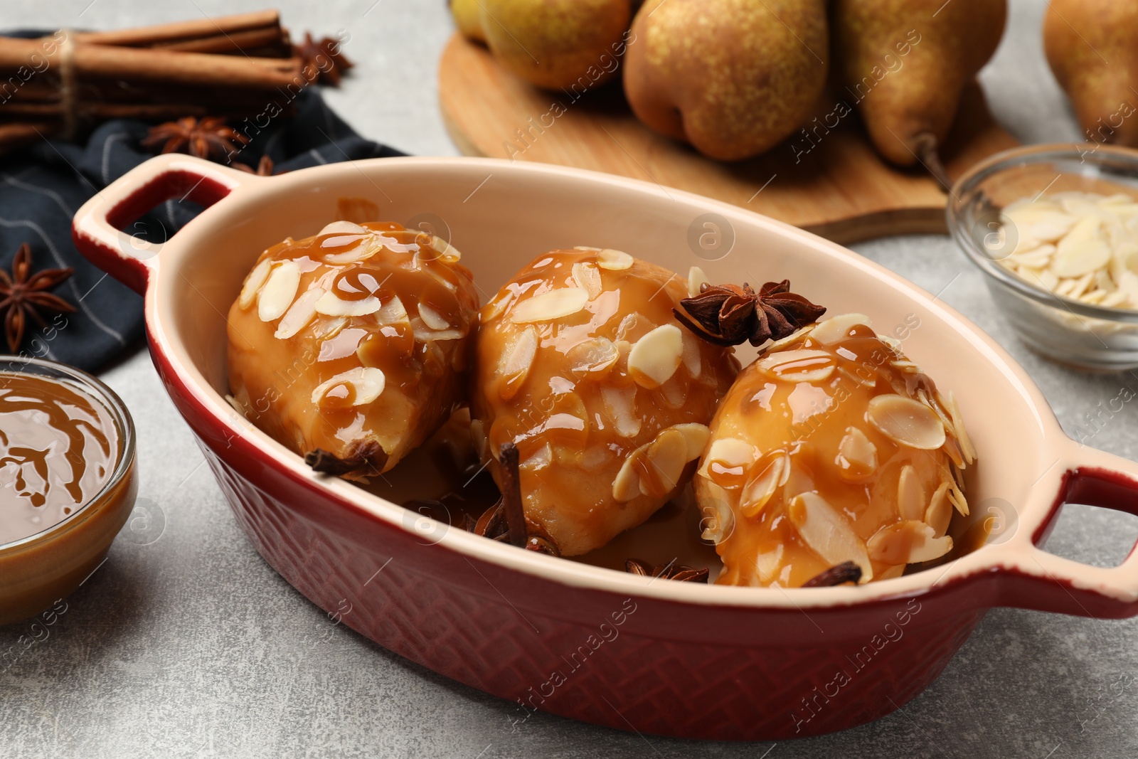 Photo of Delicious pears with caramel sauce, almond flakes and spices on grey table, closeup