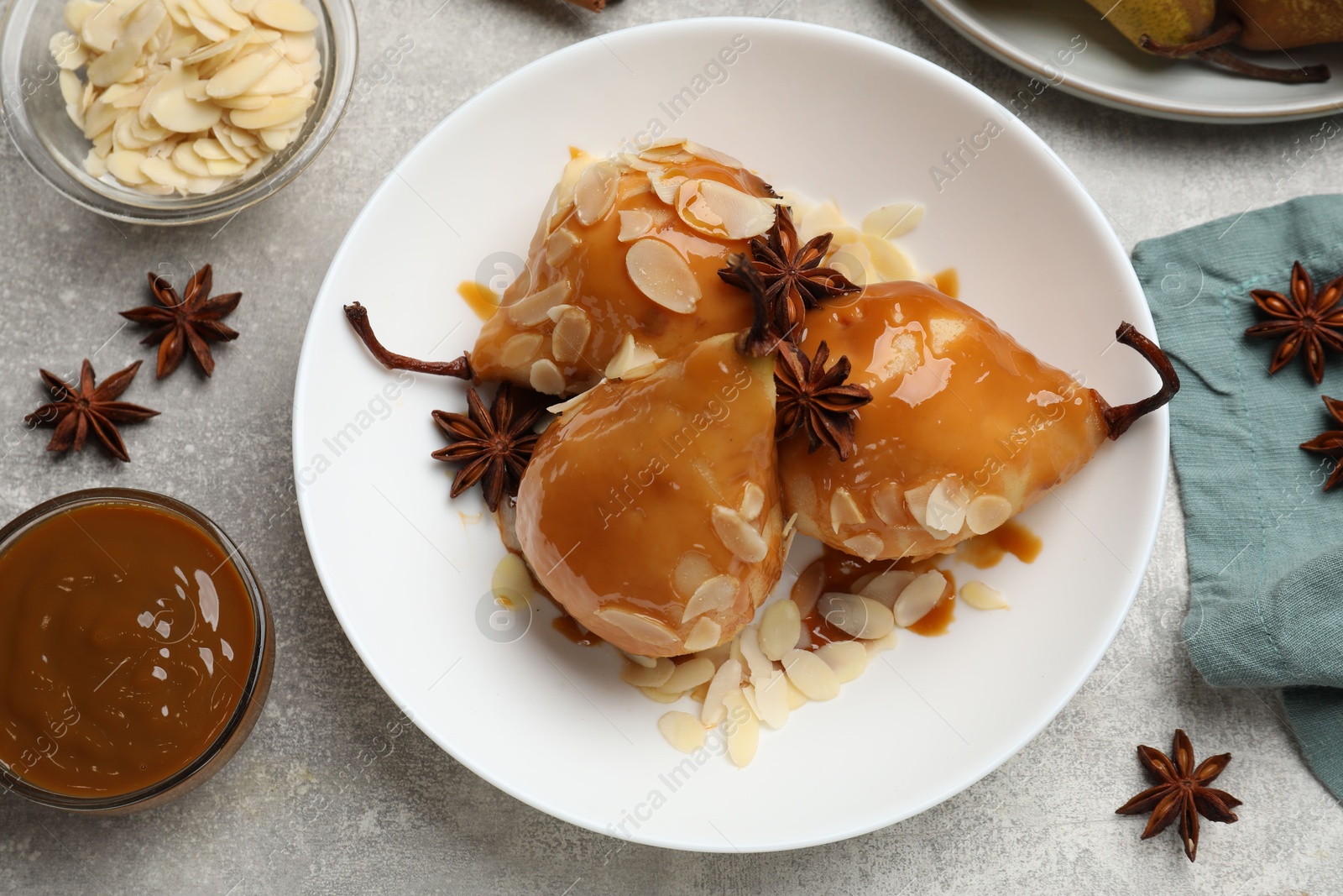 Photo of Delicious pears with caramel sauce, almond flakes and anise stars on grey table, top view