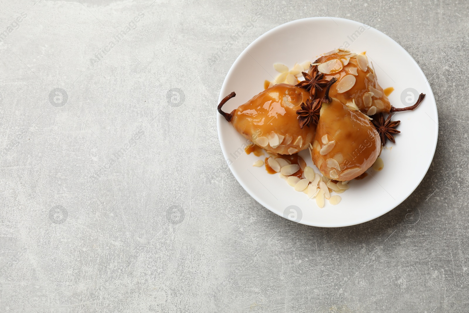 Photo of Delicious pears with caramel sauce, almond flakes and anise stars on grey table, top view. Space for text