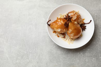 Photo of Delicious pears with caramel sauce, almond flakes and anise stars on grey table, top view. Space for text