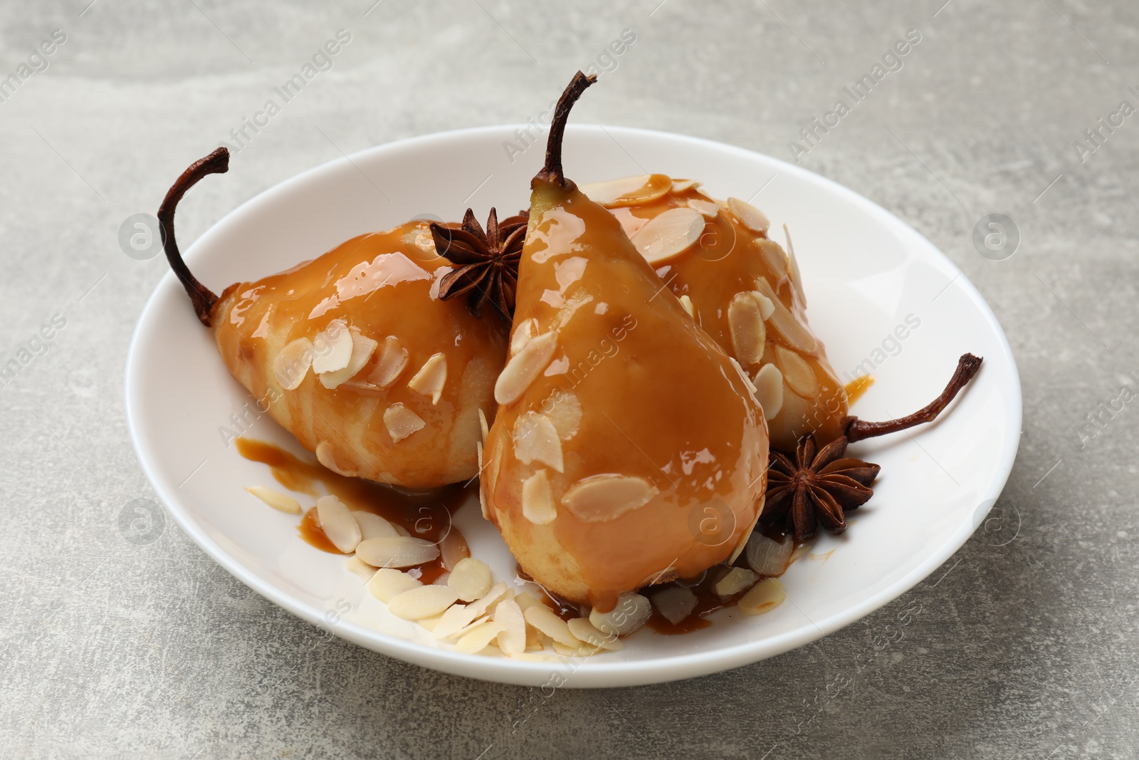 Photo of Delicious pears with caramel sauce, almond flakes and anise stars on grey table, closeup