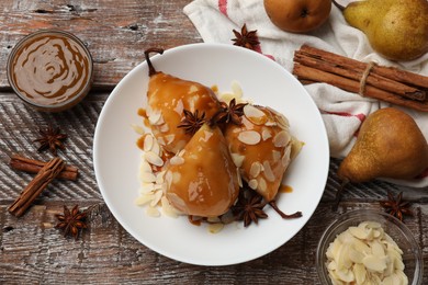 Photo of Delicious pears with caramel sauce, almond flakes and spices on wooden table, top view