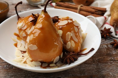 Photo of Delicious pears with caramel sauce, almond flakes and spices on wooden table, closeup