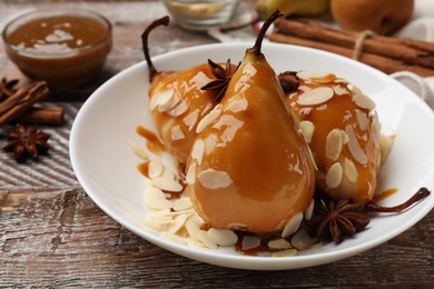 Photo of Delicious pears with caramel sauce, almond flakes and spices on wooden table, closeup