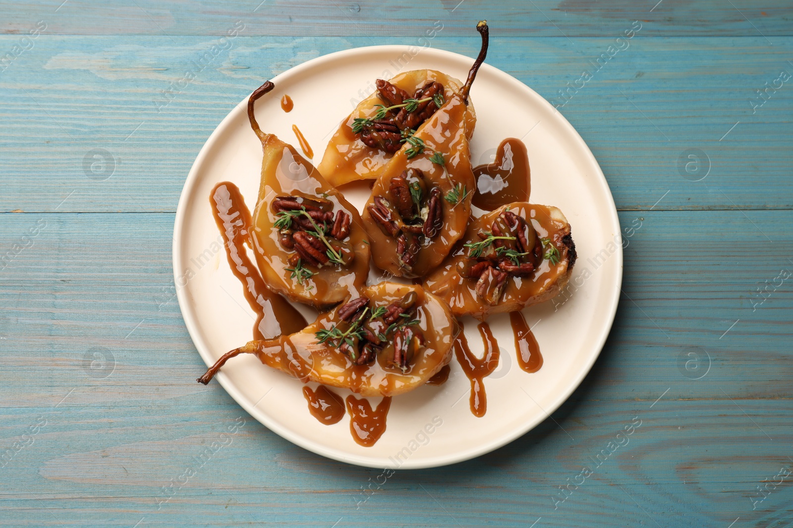 Photo of Delicious pears with caramel sauce, pecan nuts and thyme on light blue wooden table, top view