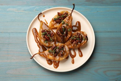 Photo of Delicious pears with caramel sauce, pecan nuts and thyme on light blue wooden table, top view