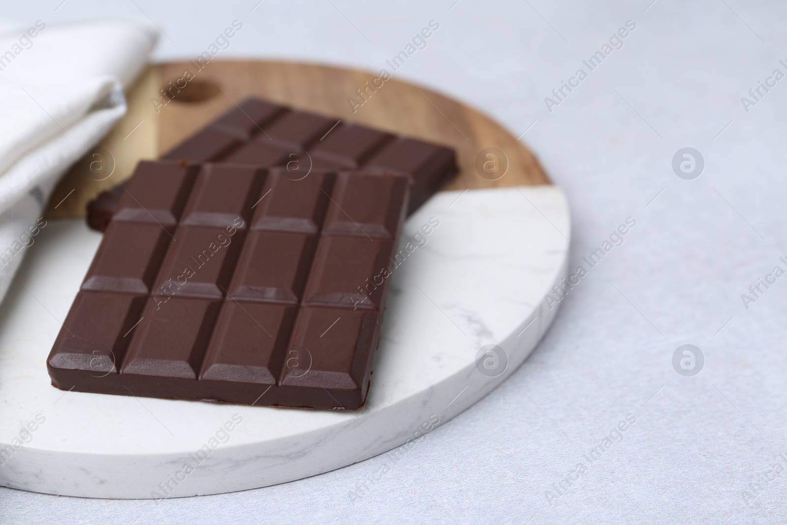 Photo of Pieces of delicious dark chocolate bar on light table, closeup. Space for text