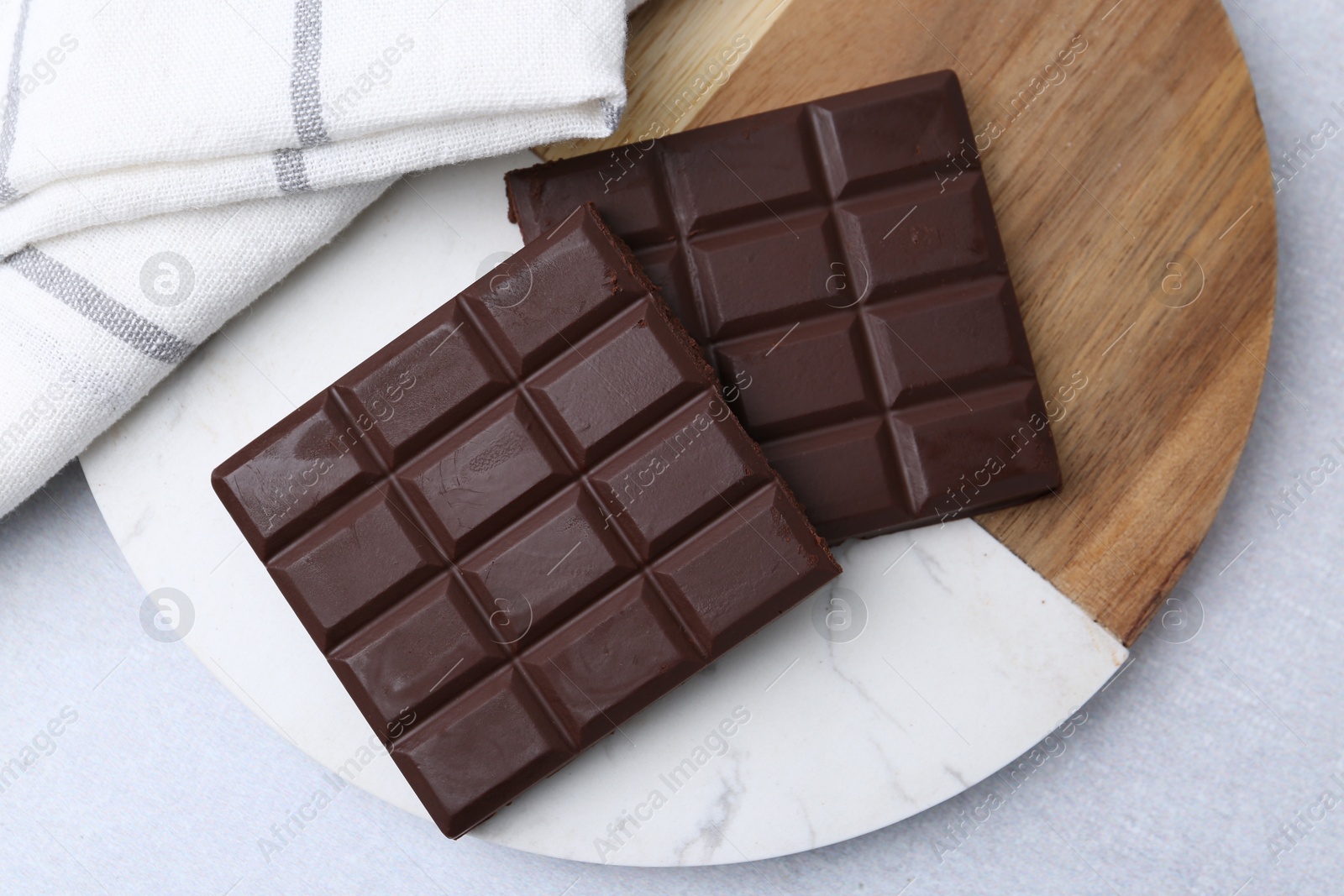 Photo of Pieces of delicious dark chocolate bar on light table, top view